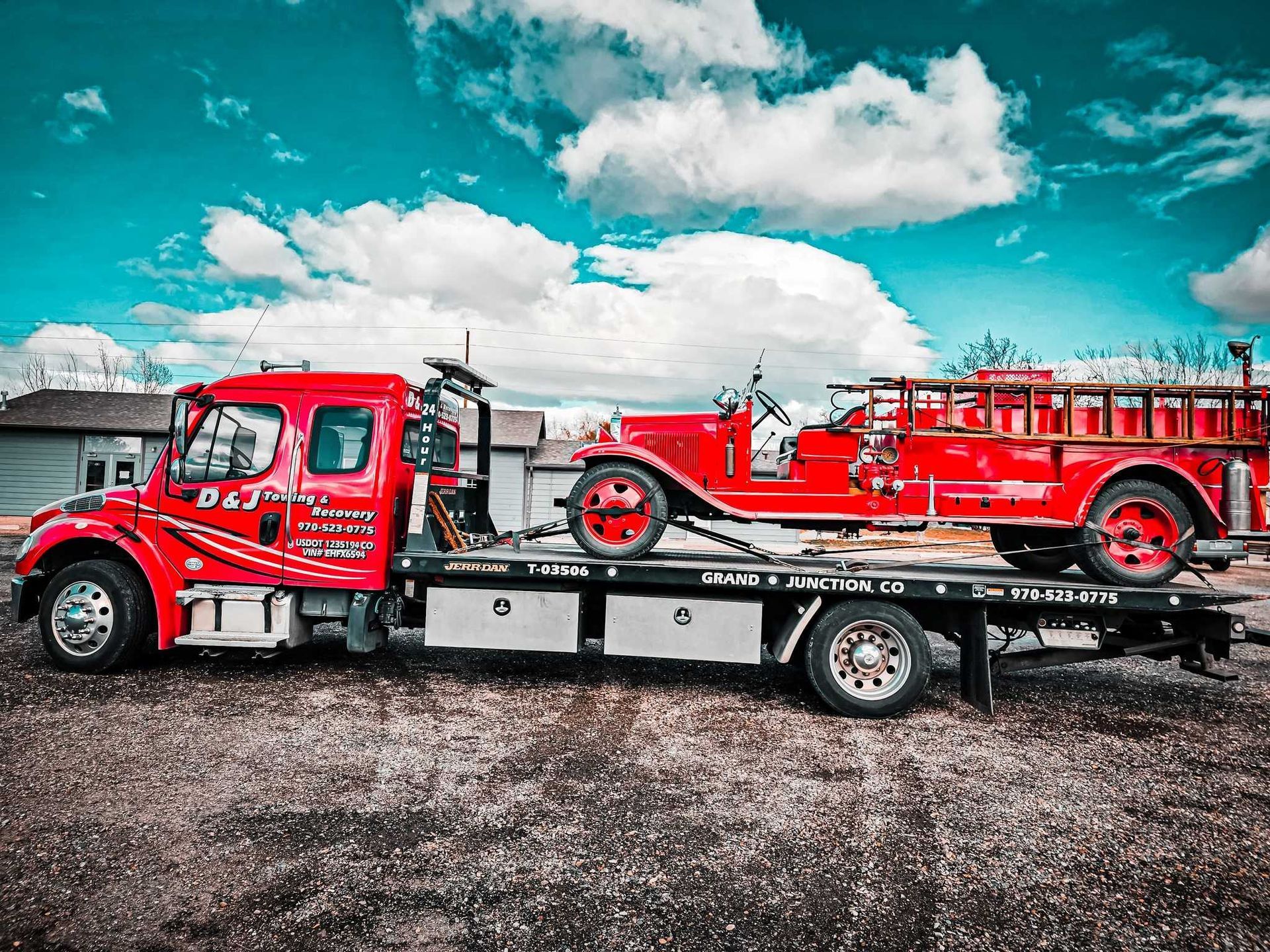 Red tow truck transporting a vintage red fire truck on a sunny day.