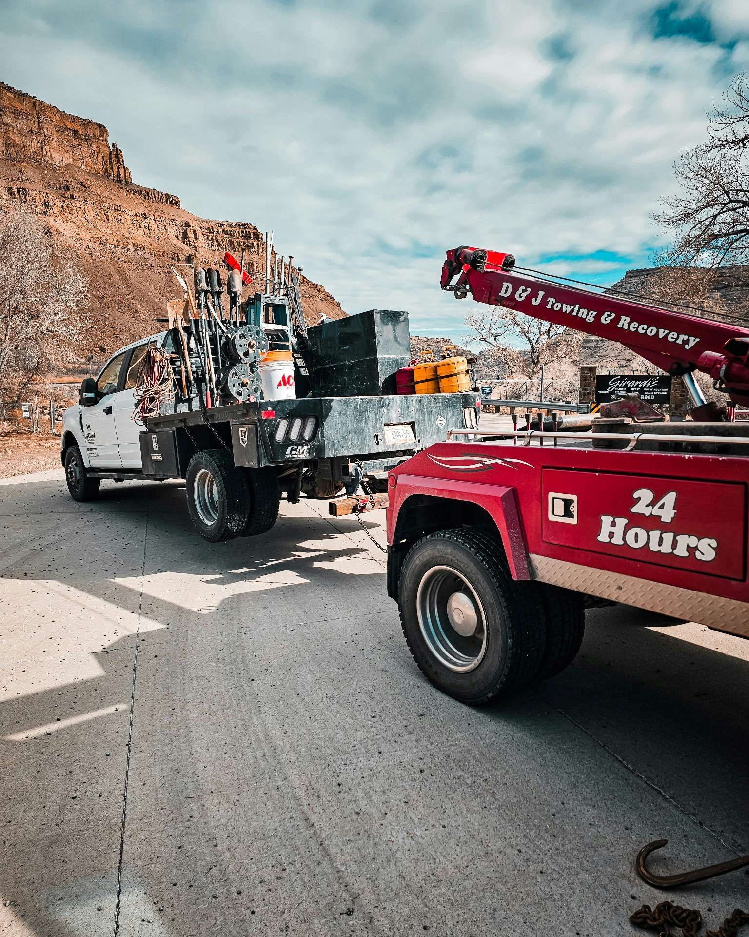 Tow trucks hook up on a road in a desert setting with rocky cliffs in the background.