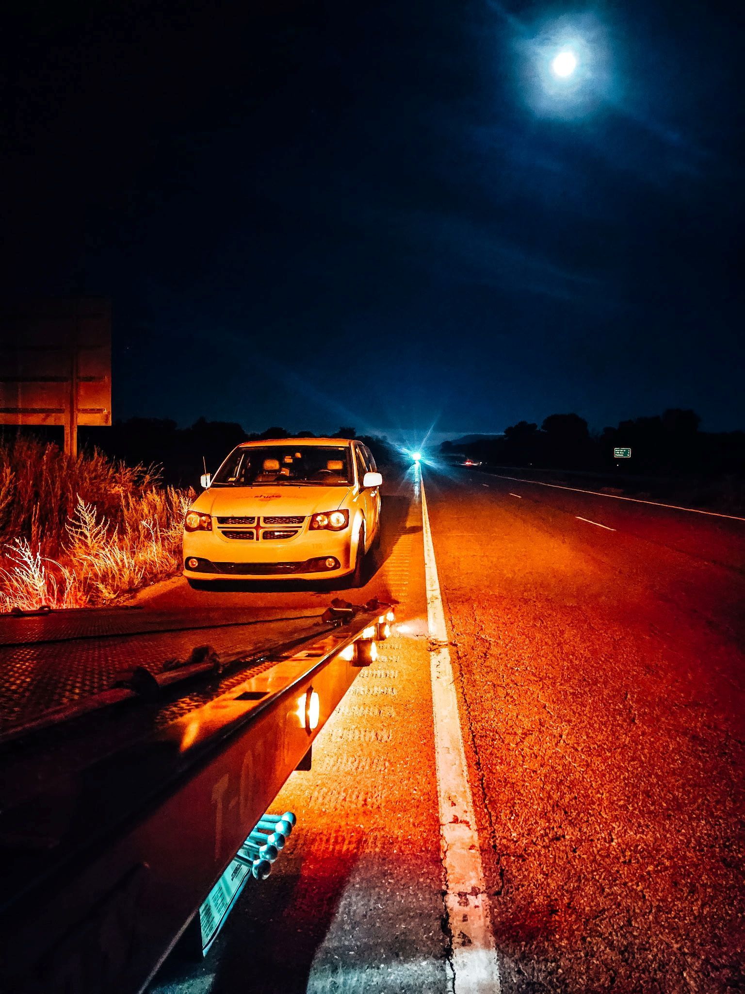 Car parked on a dark highway at night, illuminated by headlights and the moon.