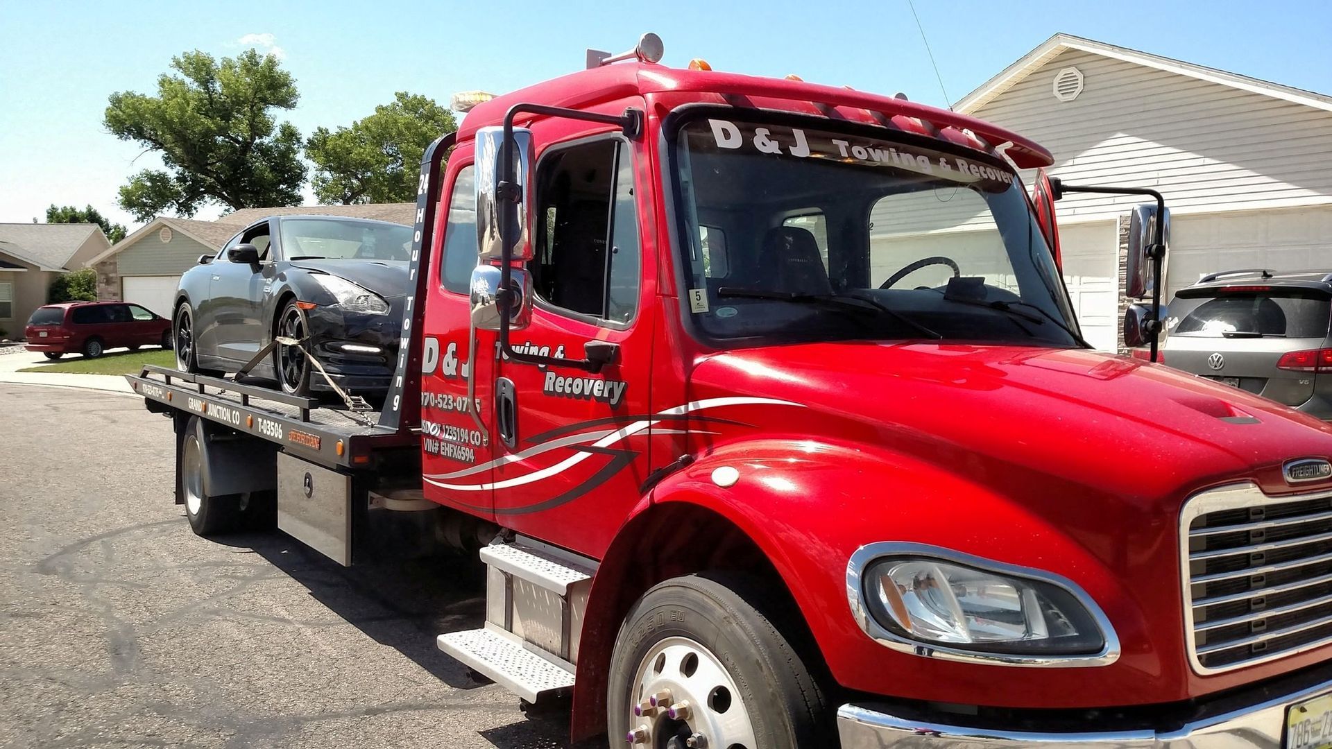 Red tow truck transporting a black car on a sunny day.
