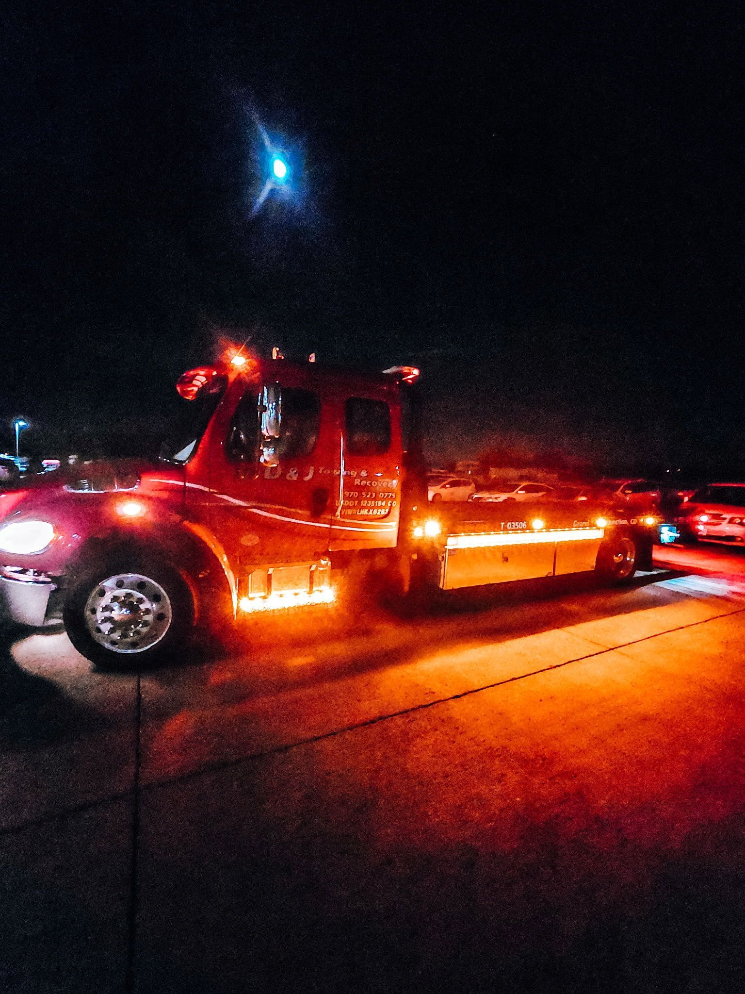 Red tow truck at night with bright lights illuminating the truck and the ground.