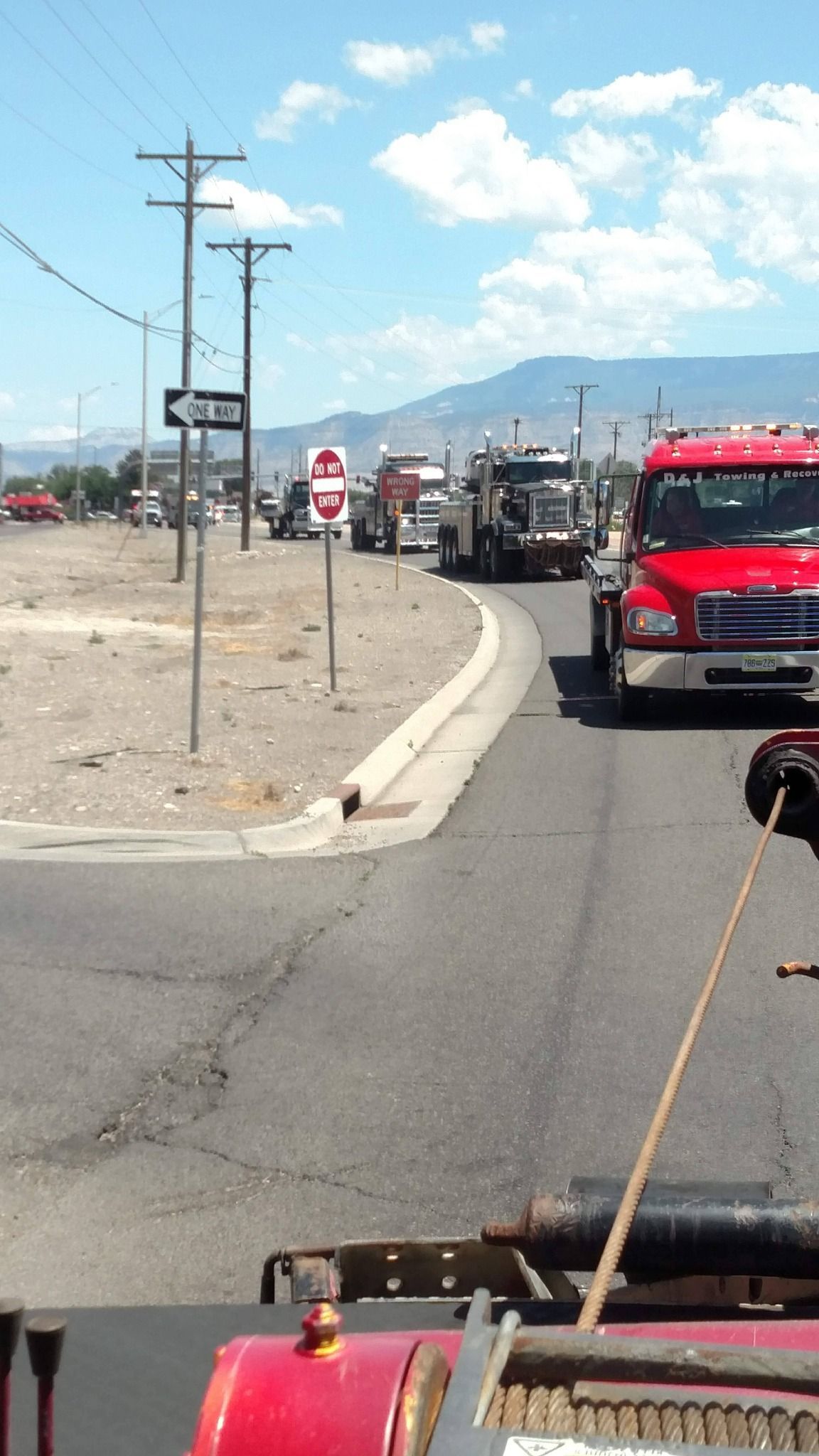 Several tow trucks on a road, likely at an accident scene. Sunny day with mountains in the background.