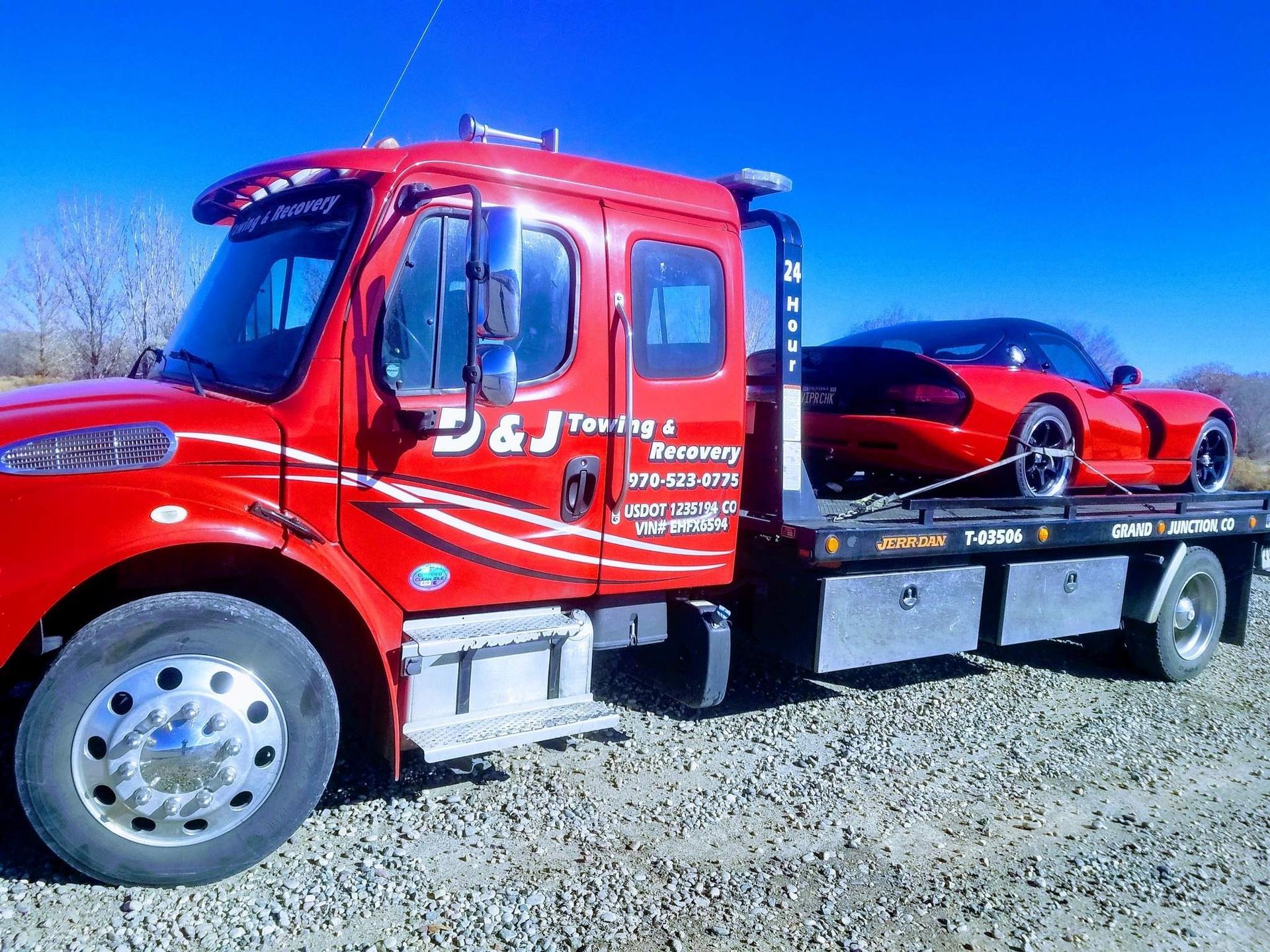 Red tow truck with a red sports car on its flatbed, under a blue sky.