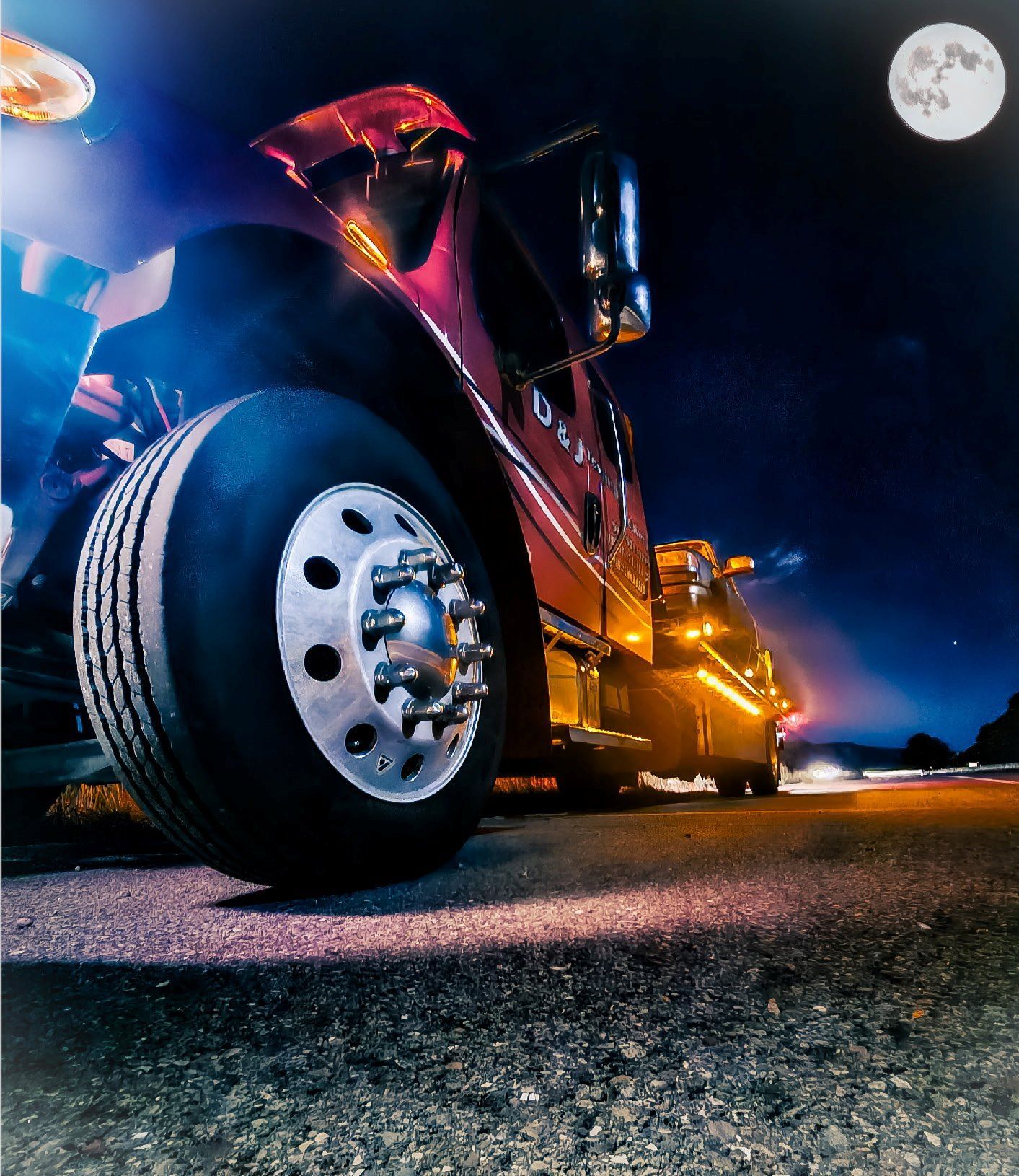 Semi-truck on a road at night with the moon in the sky.