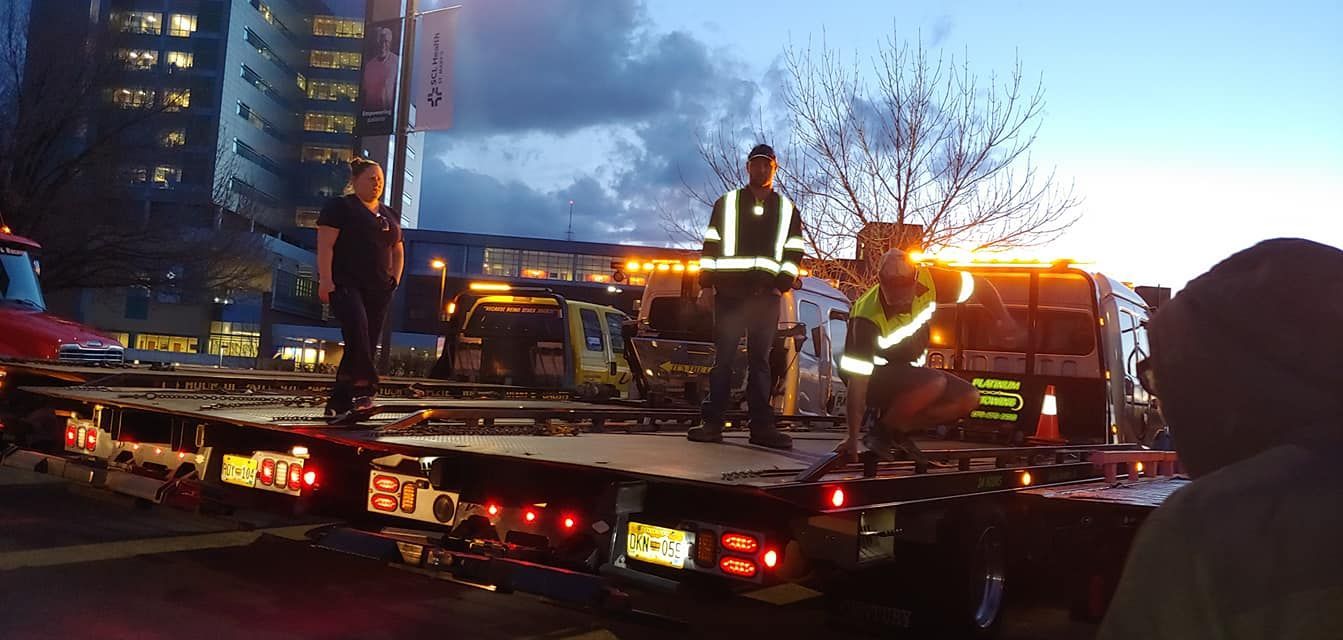 People on a large flatbed trailer with a vehicle, lit by emergency lights, next to a building.