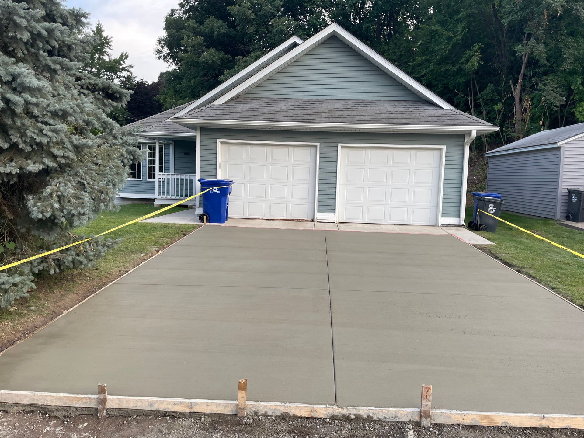 Freshly poured concrete driveway in front of a blue house with two garage doors and a small yard.