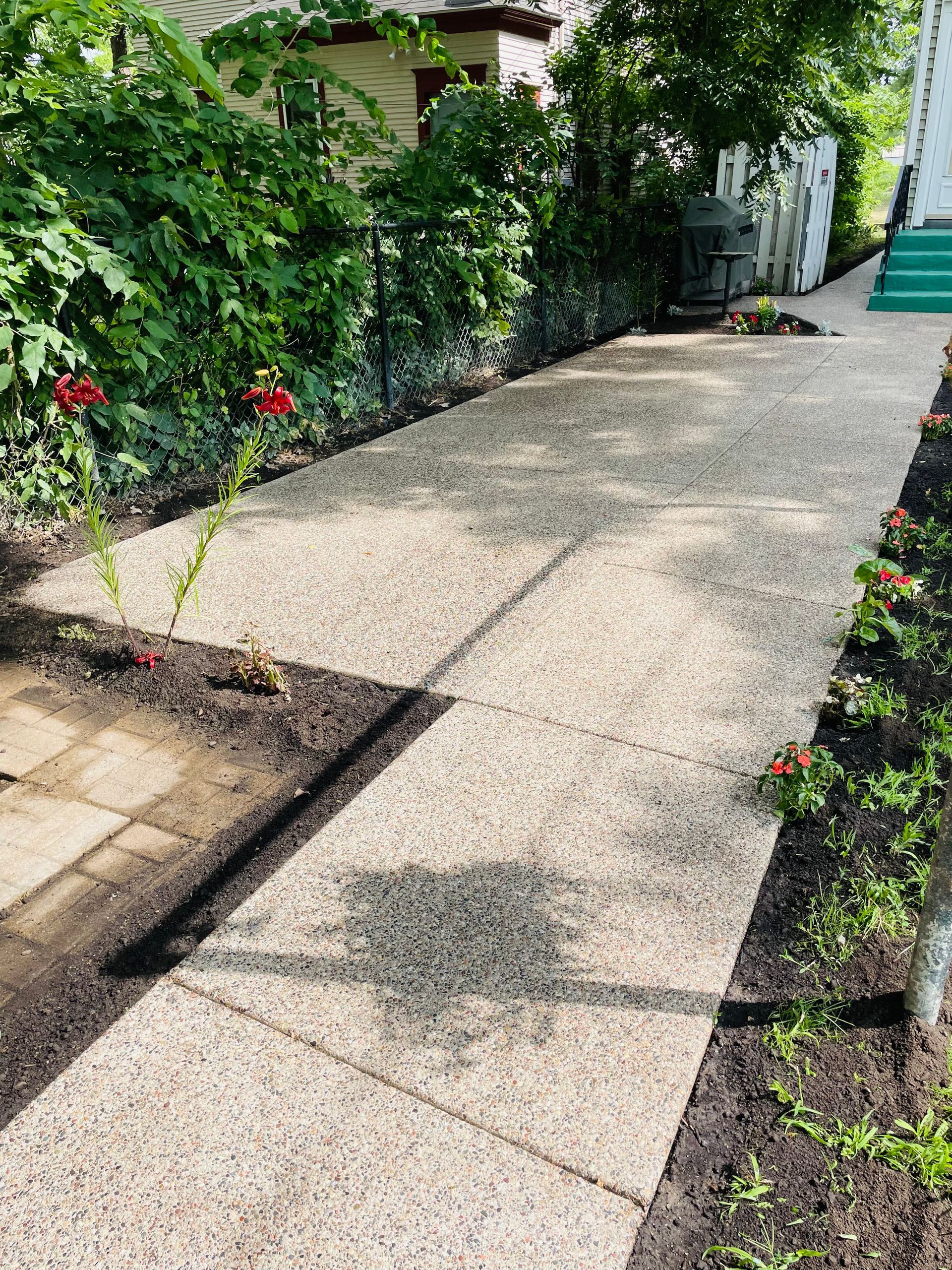 A concrete walkway leading to a house with flowers on the side.