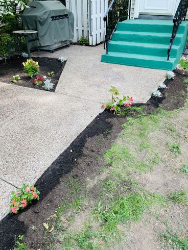 A patio with a grill , stairs and flowers in front of a house.