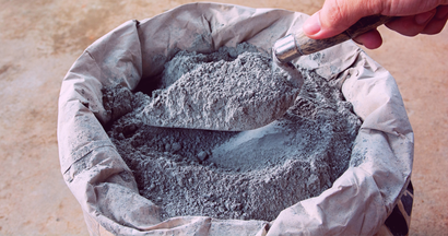 A person is holding a shovel over a bag of cement.