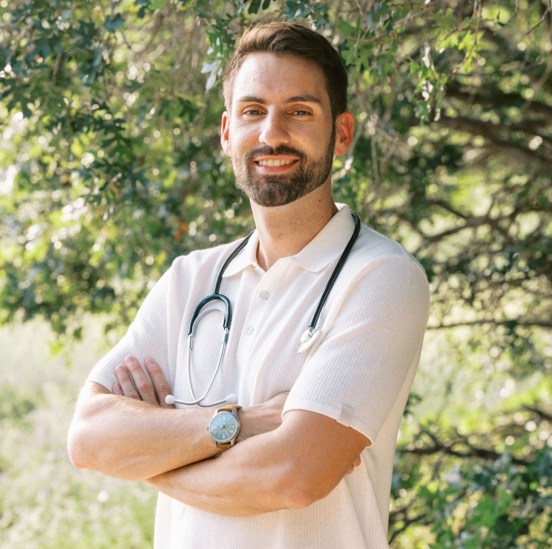 A man with a stethoscope around his neck is standing with his arms crossed.