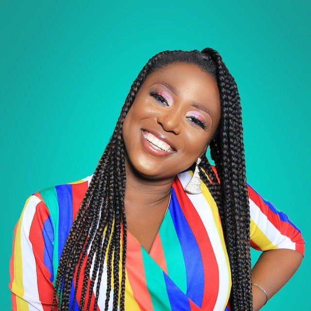 A woman with braids is wearing a colorful striped shirt and smiling.