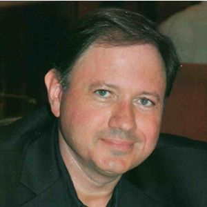 A man in a black suit is smiling for the camera.