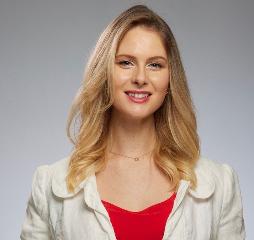 Rachel wearing a white jacket and a red top is smiling for the camera.