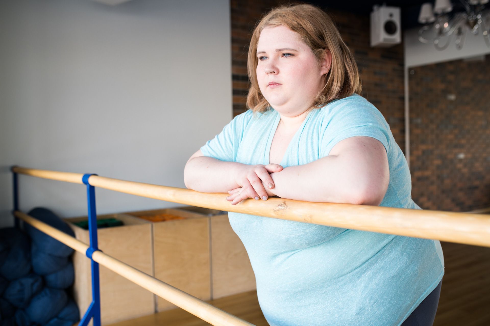 A woman is leaning on a bar in a dance studio.