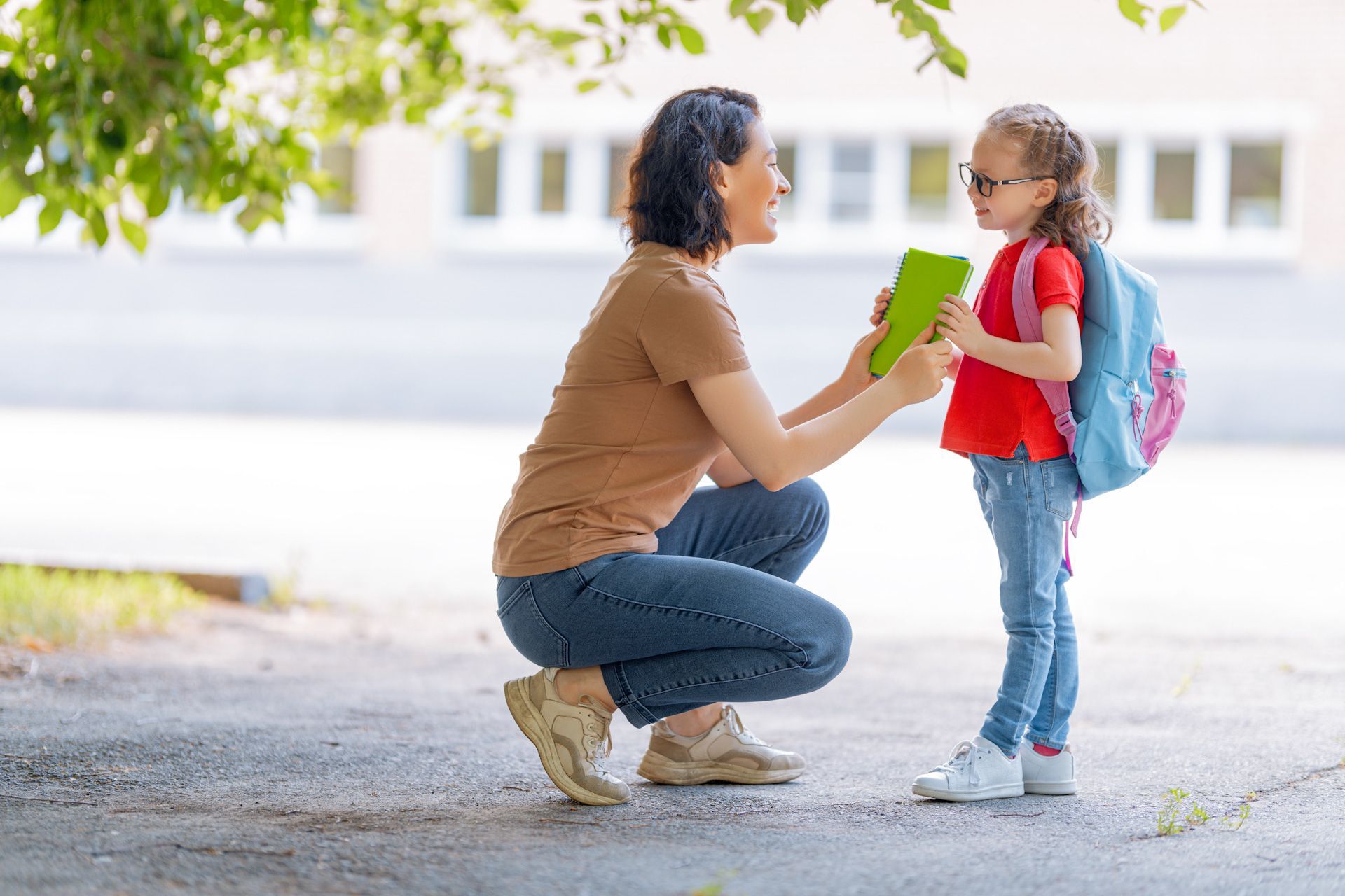 A woman is kneeling down next to a little girl holding a tablet.