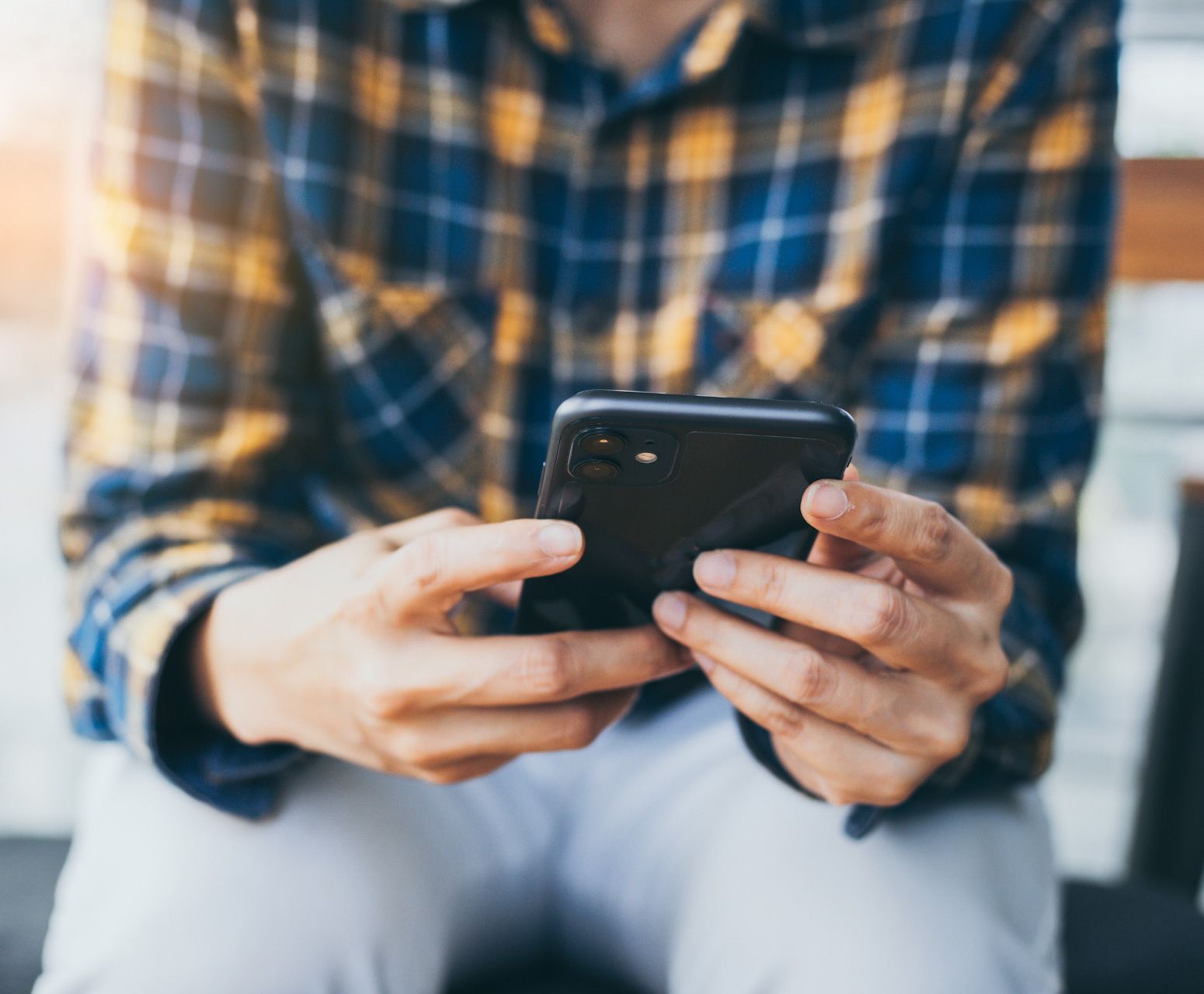 A man in a plaid shirt is holding a cell phone in his hands.