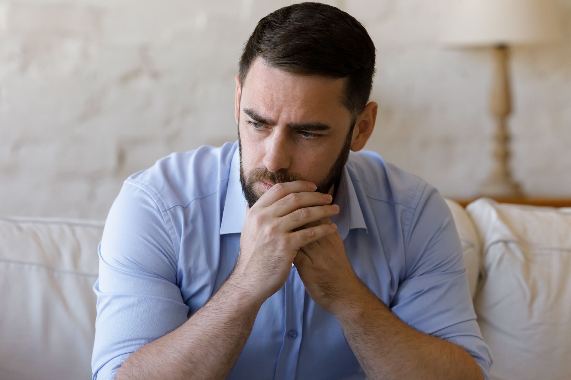 A man with a beard is sitting on a couch with his hands on his chin.