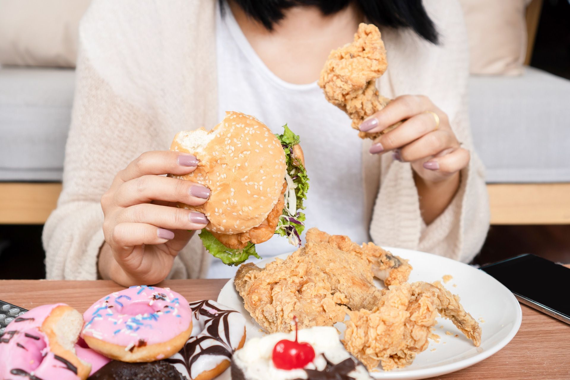 A woman is sitting at a table eating a hamburger and fried chicken.