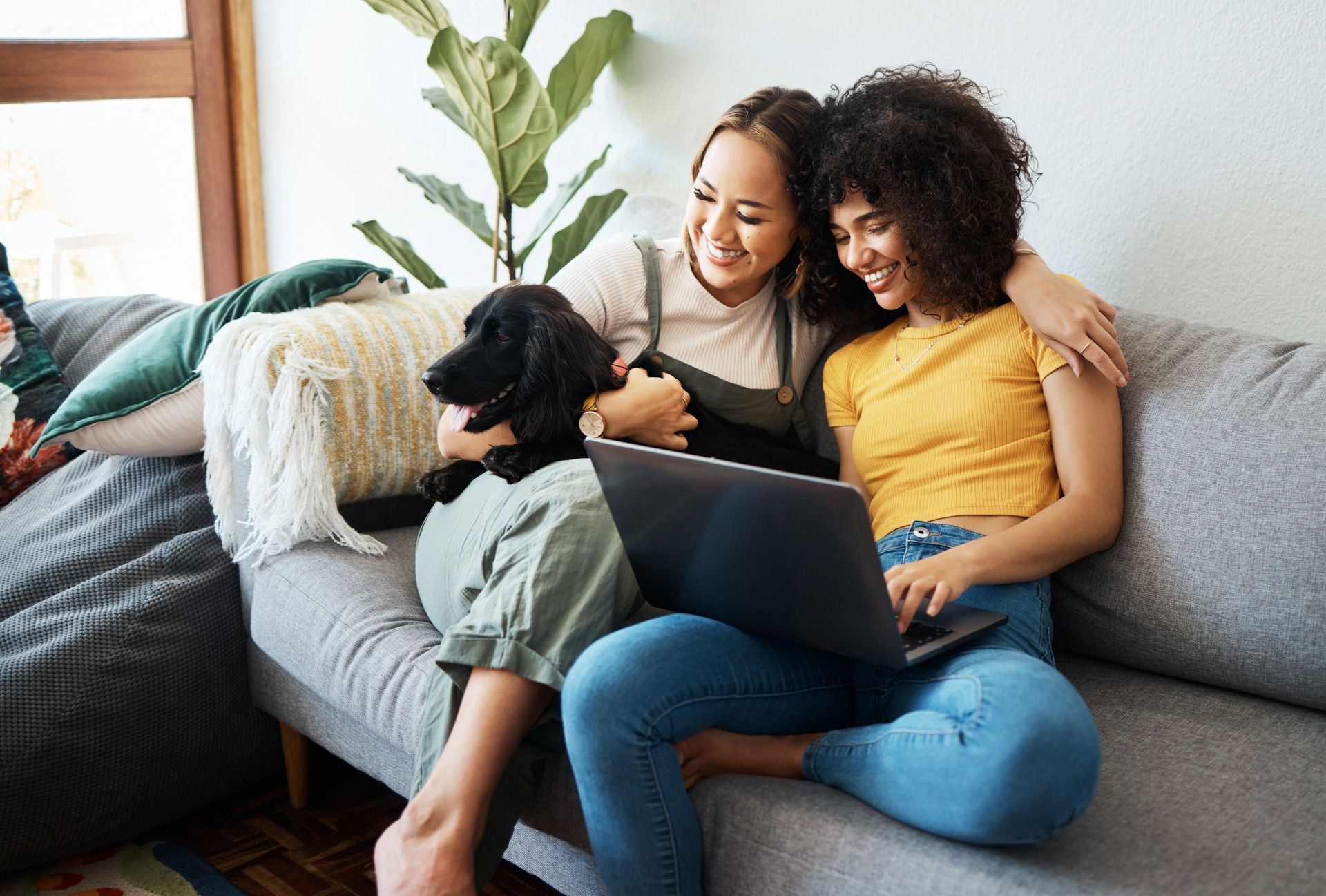 An LGBTQ couple are sitting on a couch looking at a laptop.