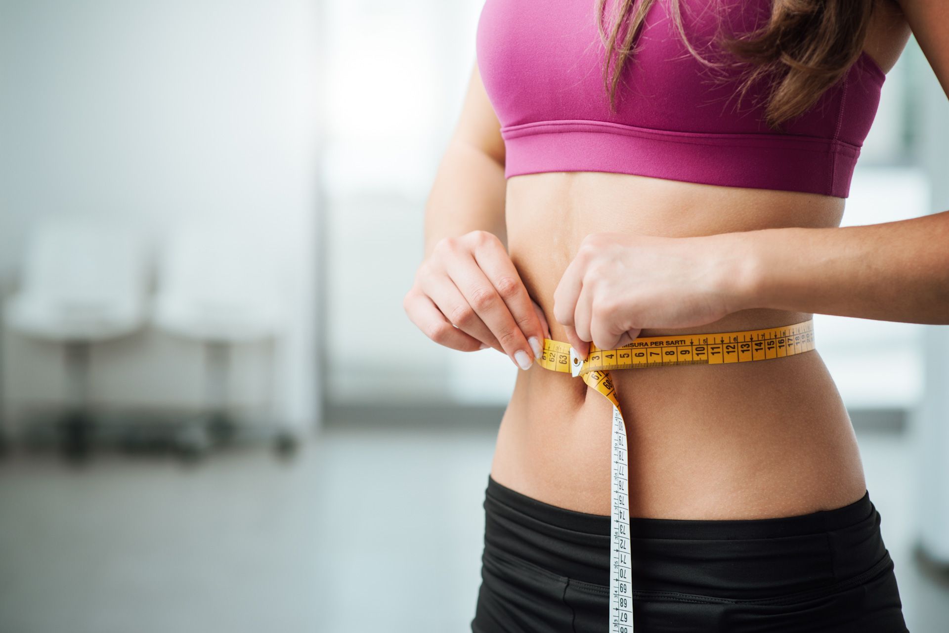 A woman is measuring her waist with a tape measure.