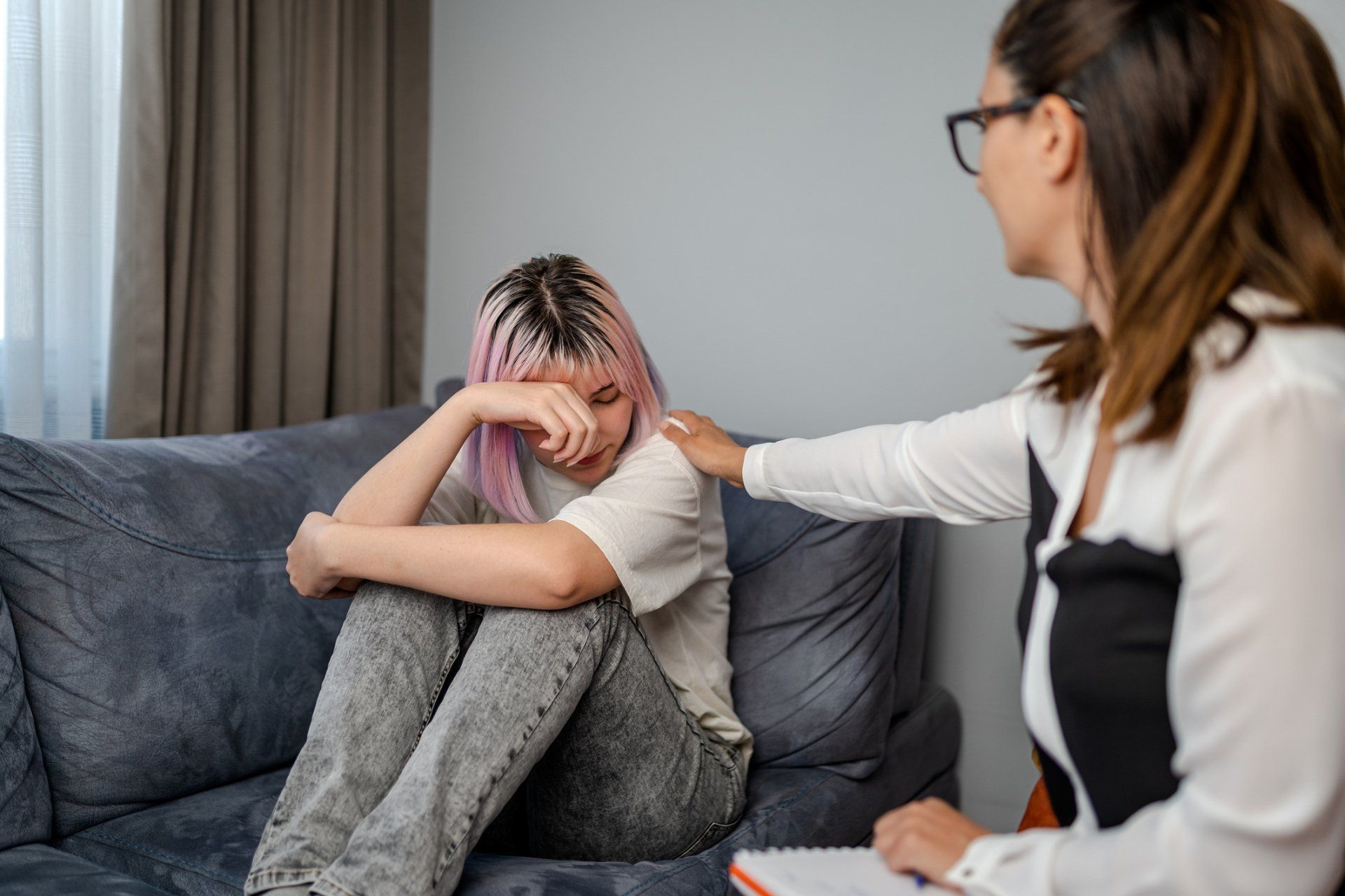 A woman with pink hair is sitting on a couch talking to a psychologist.