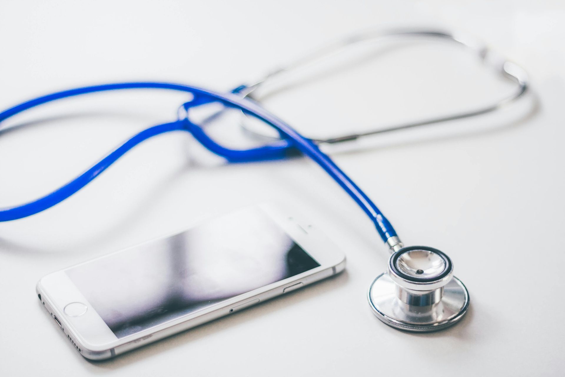 White smartphone and blue stethoscope on a white surface, suggesting healthcare and technology.