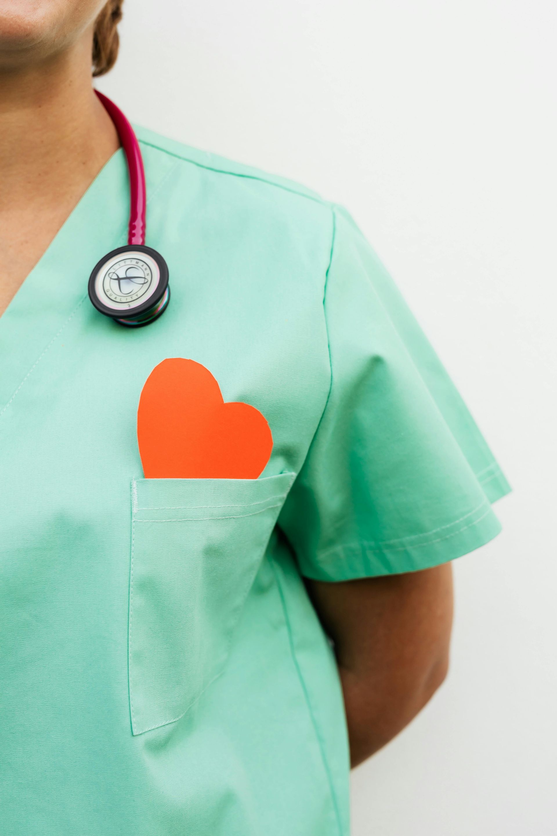 Nurse in green scrubs with a stethoscope, red heart in pocket.