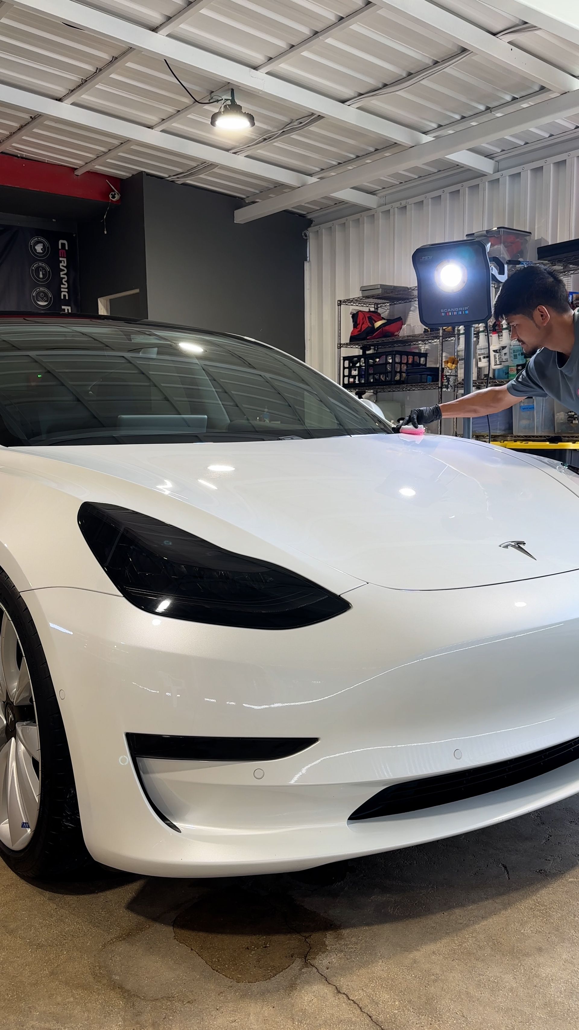A man is standing next to a white tesla model 3 in a garage.
