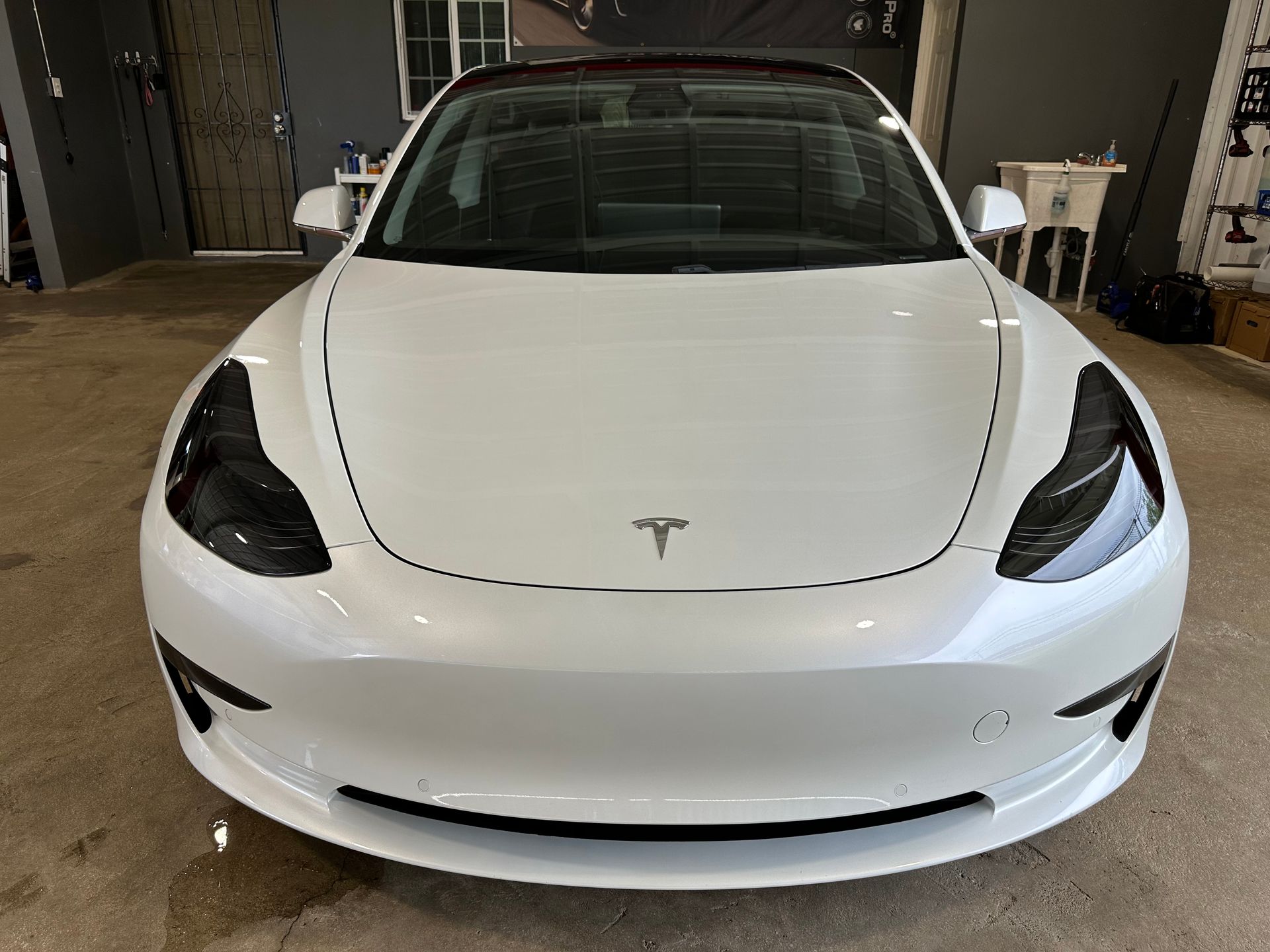 A white tesla model 3 is parked in a garage.