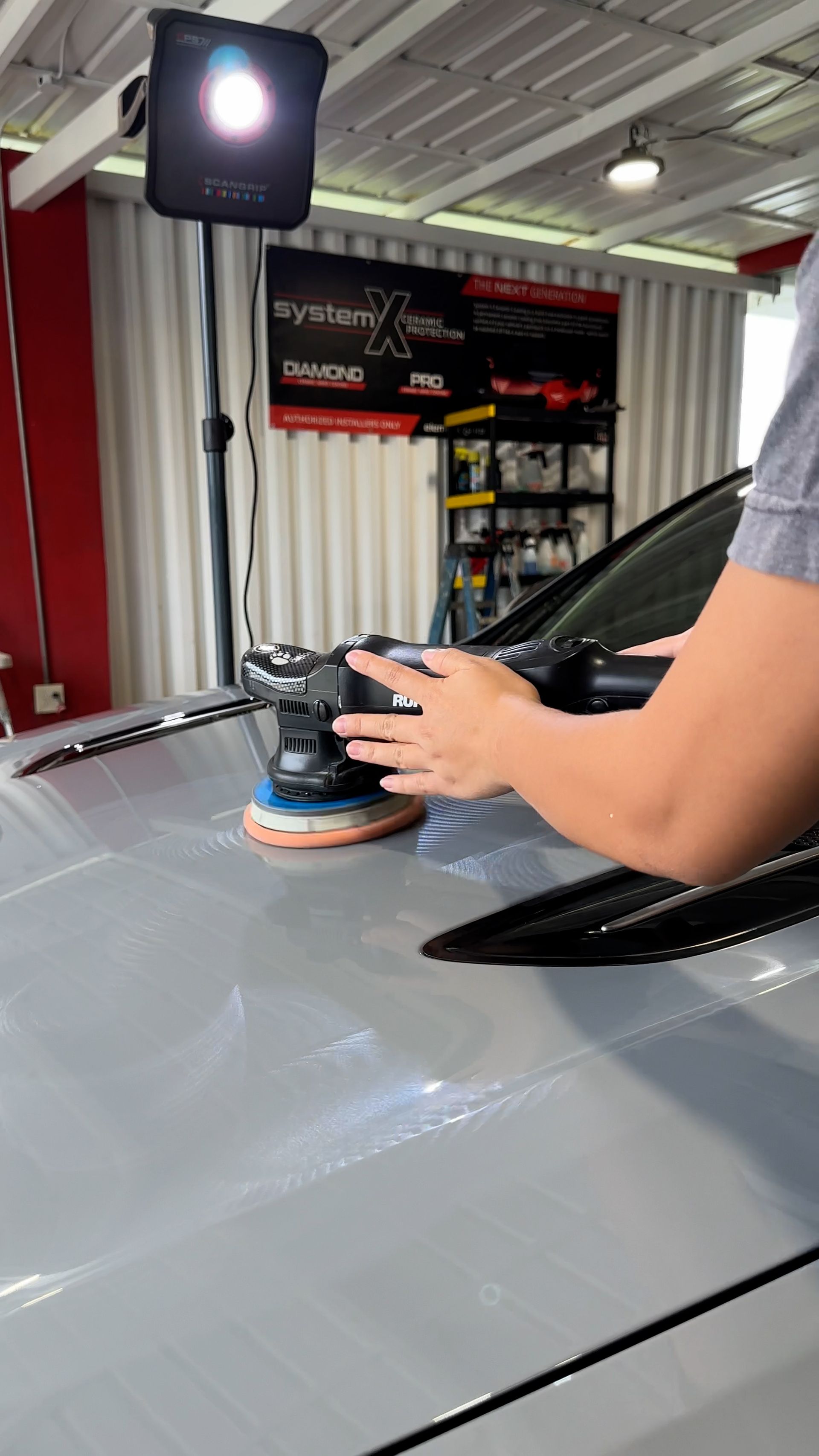 A person is polishing the hood of a car with a machine.