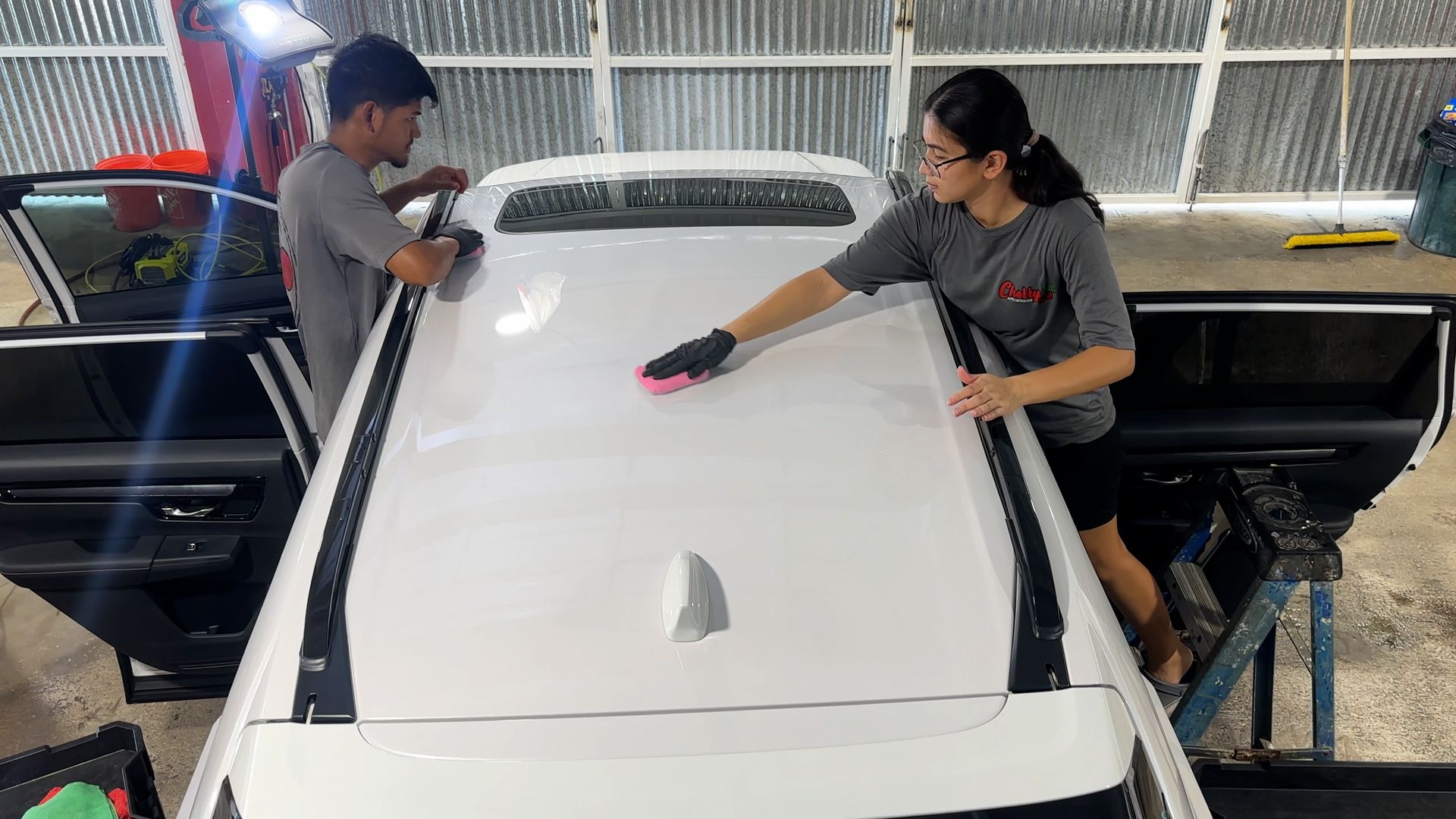 A man and a woman are cleaning the roof of a white car.