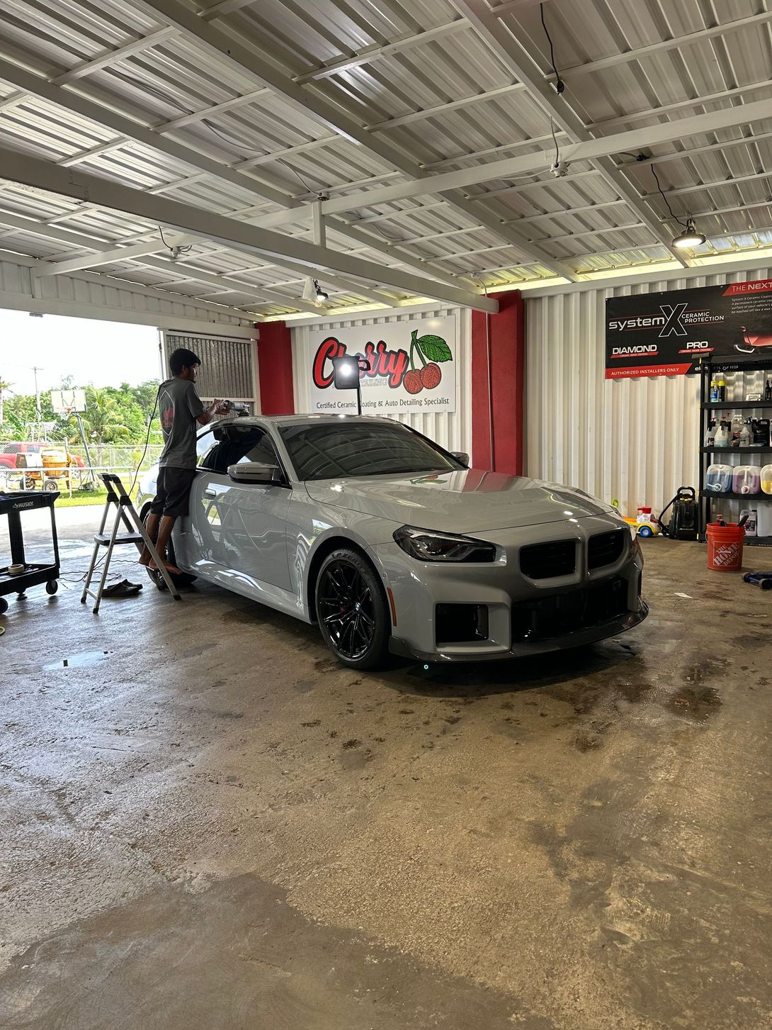 A man is standing next to a white car in a garage.