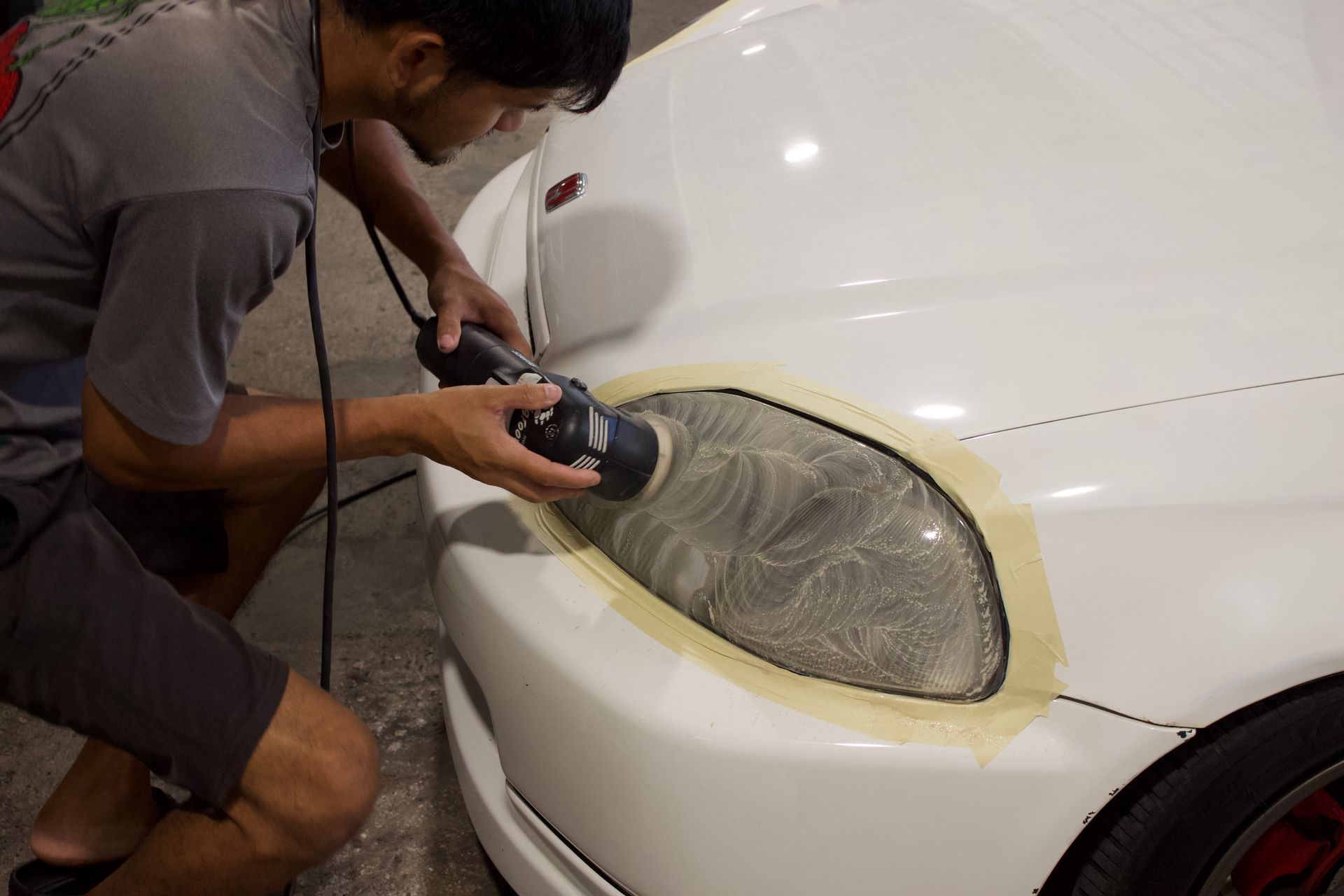 A man is standing next to a white car in a garage.