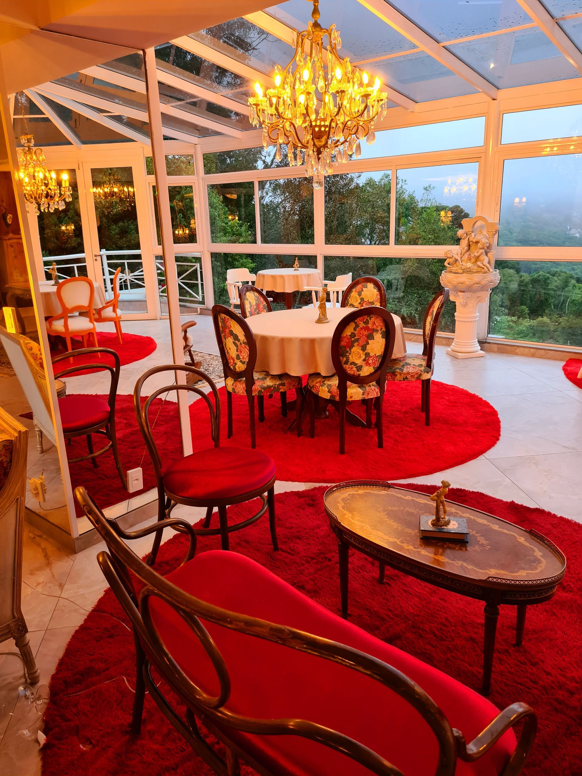 Uma sala de estar com um sofá vermelho, cadeiras, mesas e um lustre.