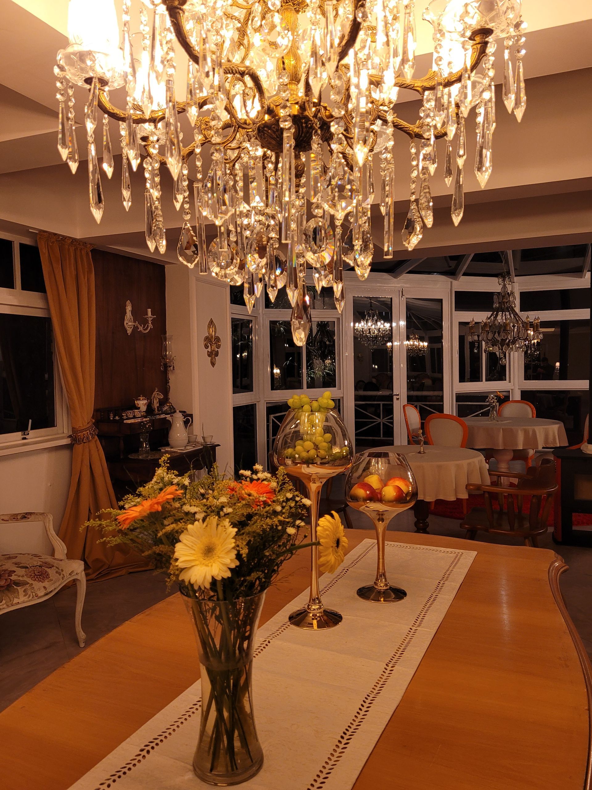 Uma mesa com um vaso de flores e uma tigela de frutas sob um lustre.