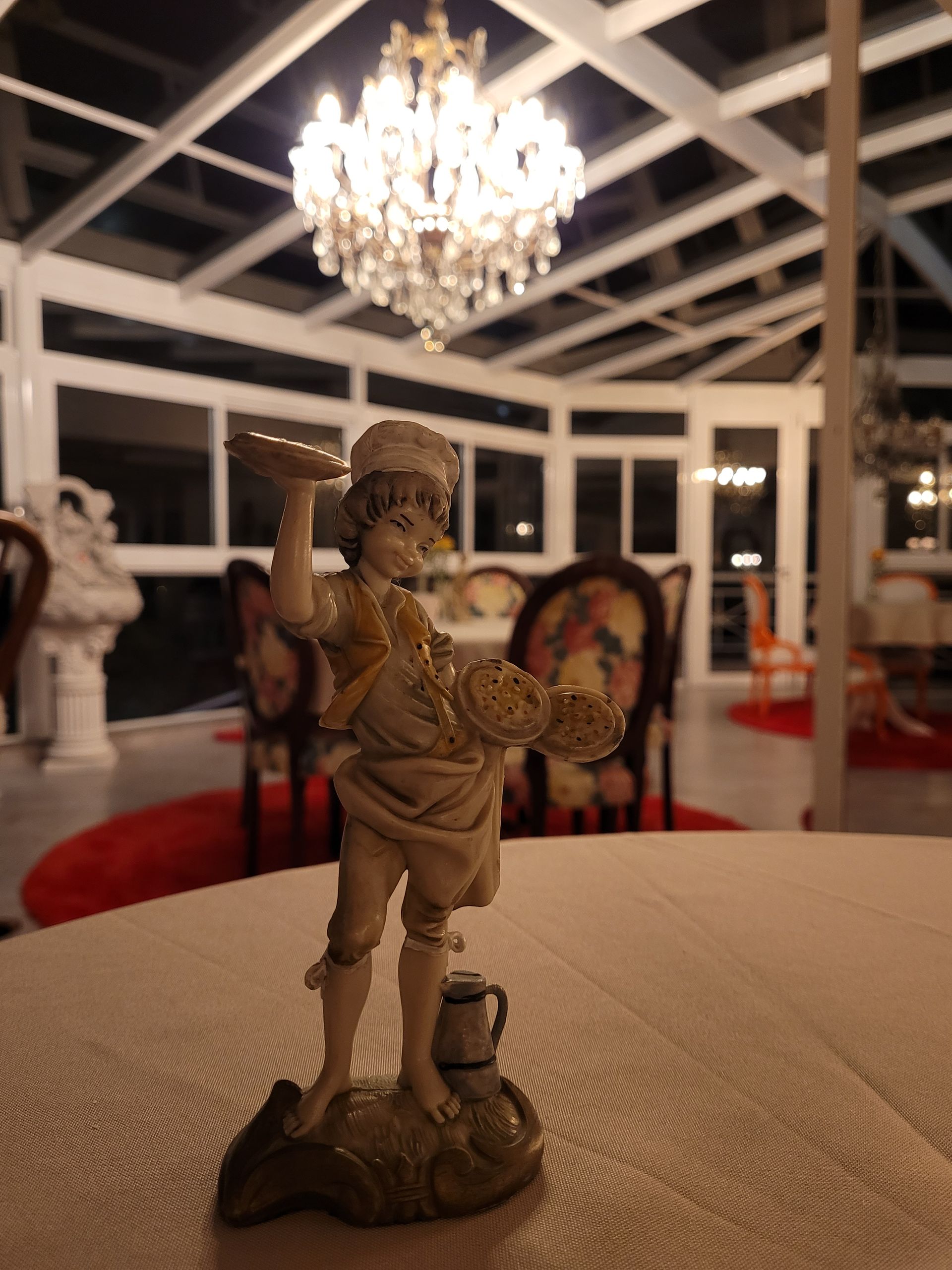 Uma estátua de um homem em pé sobre uma mesa com um lustre ao fundo