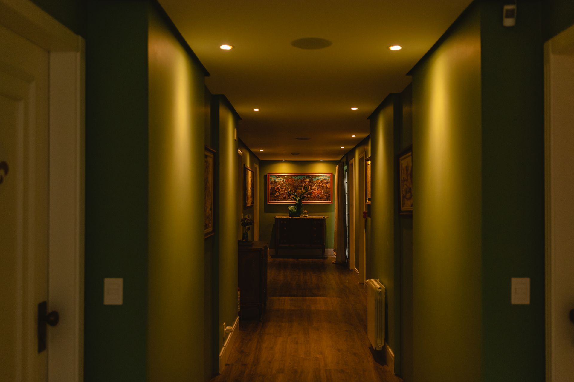 Um longo corredor com paredes verdes e pisos de madeira em uma casa.