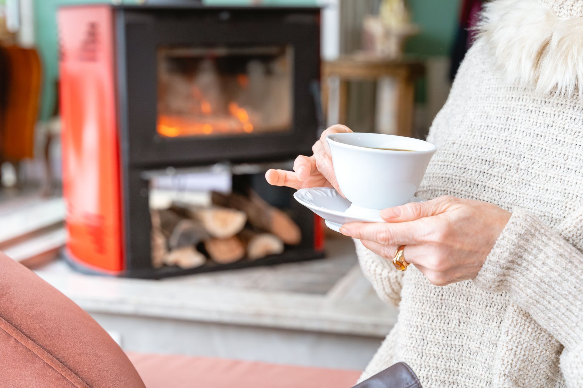 Uma mulher está segurando uma xícara de café em frente à lareira.