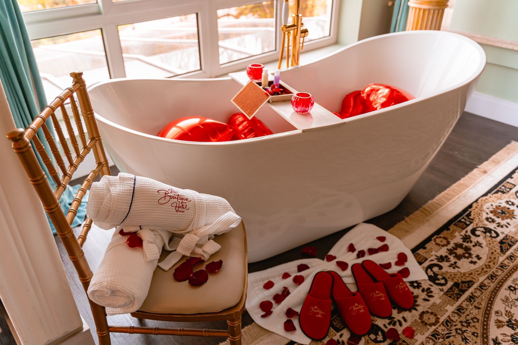 Uma banheira cheia de cobertores vermelhos e pétalas de rosa ao lado de uma cadeira.
