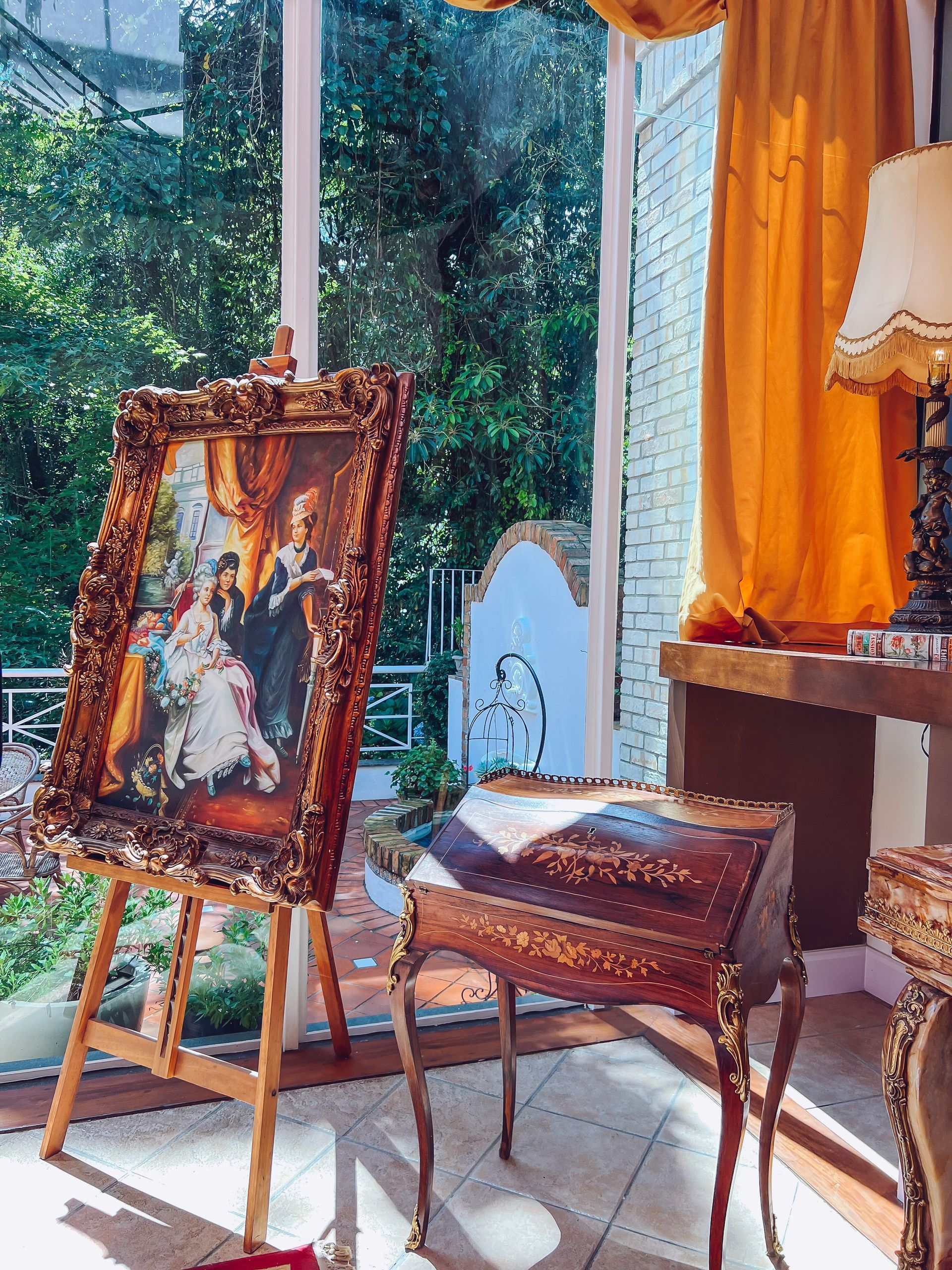 Uma pintura em um cavalete em uma sala de estar ao lado de uma janela.