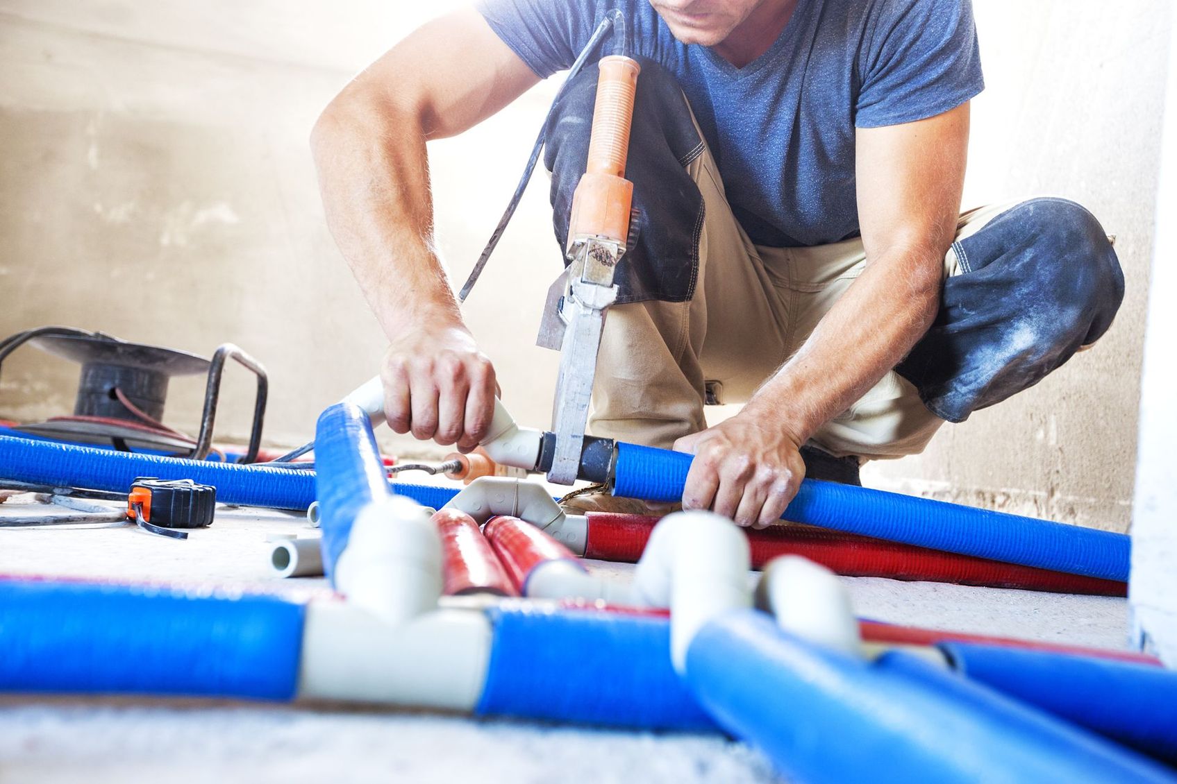 A man is kneeling on the floor working on pipes.