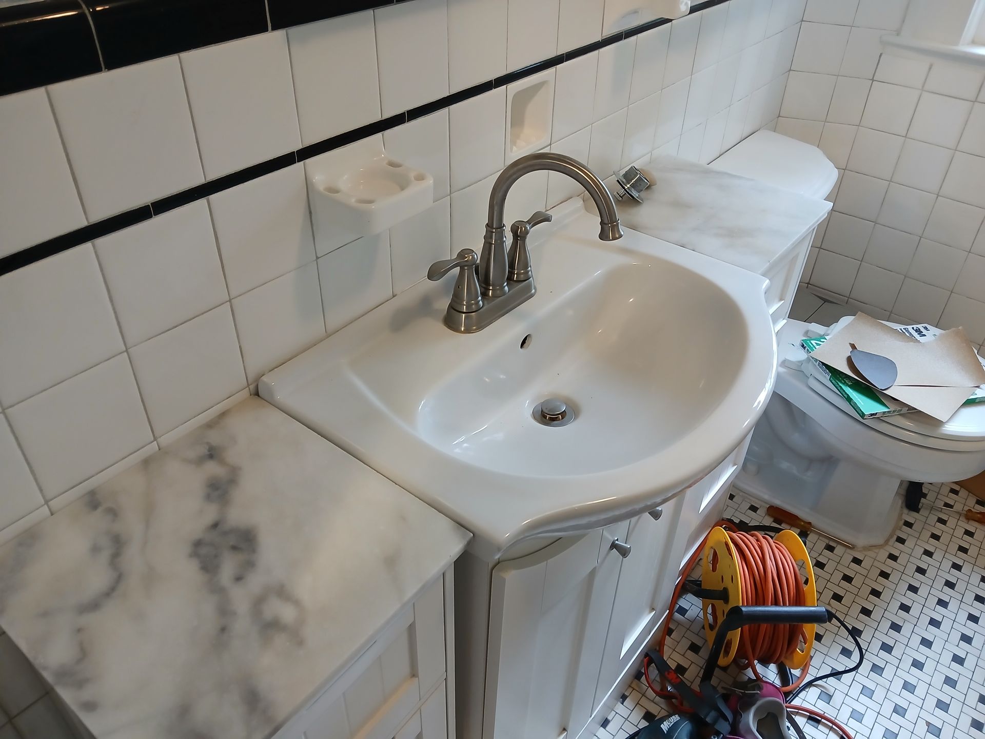 A bathroom with a sink and toilet and a hose on the floor