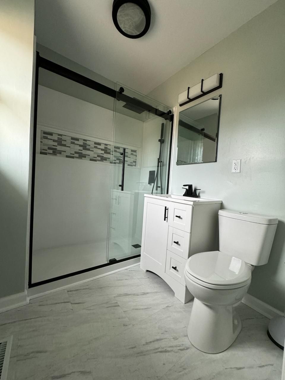 A bathroom with a toilet , sink , shower and mirror.