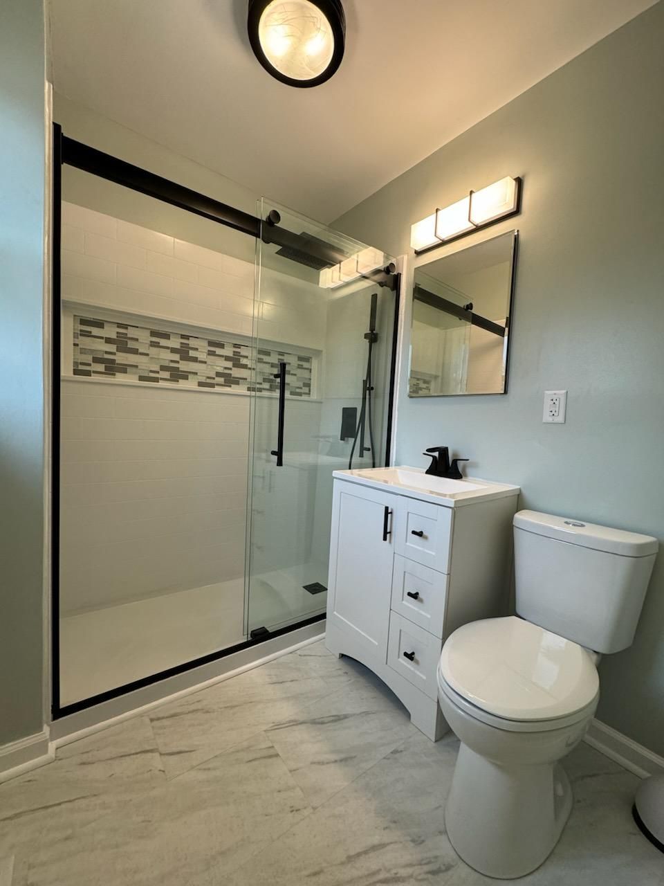 A bathroom with a toilet , sink , shower and mirror