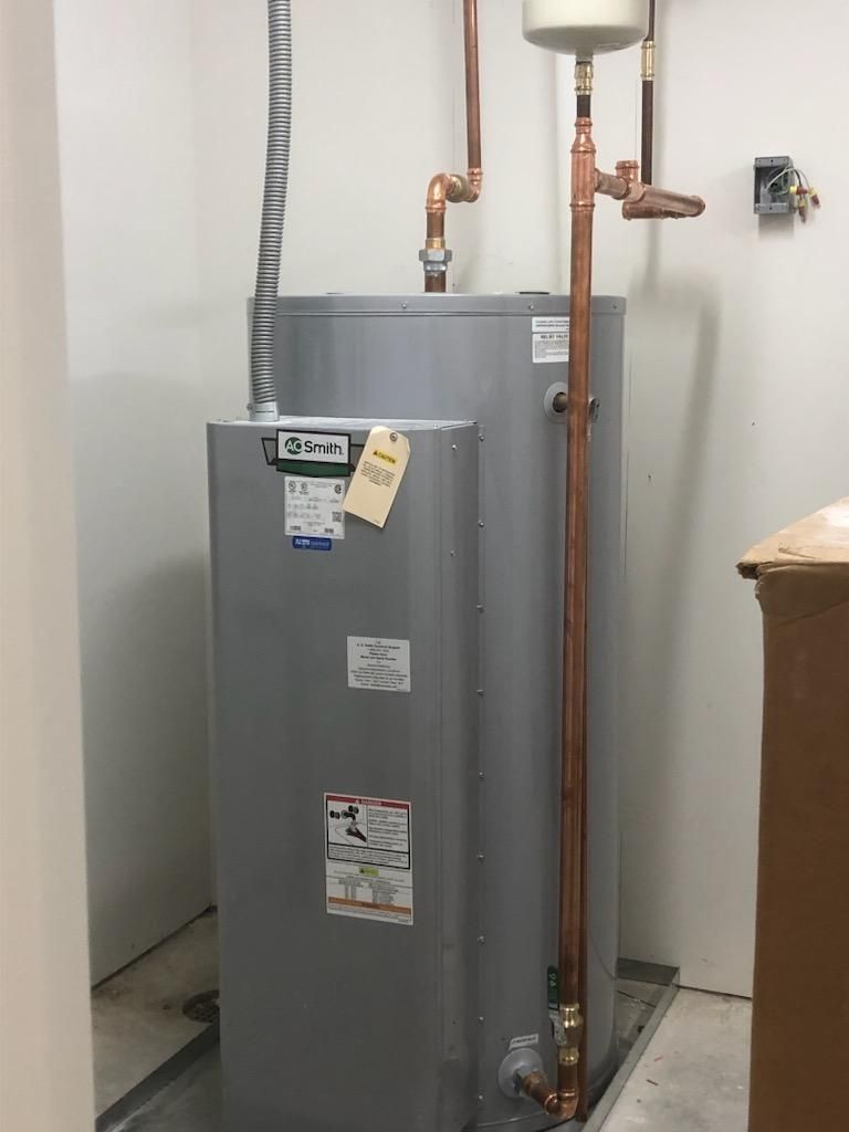 A water heater is sitting in a room next to a copper pipe.