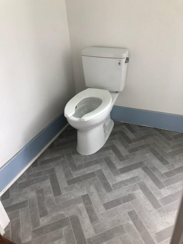 A toilet is sitting on a herringbone floor in a bathroom.