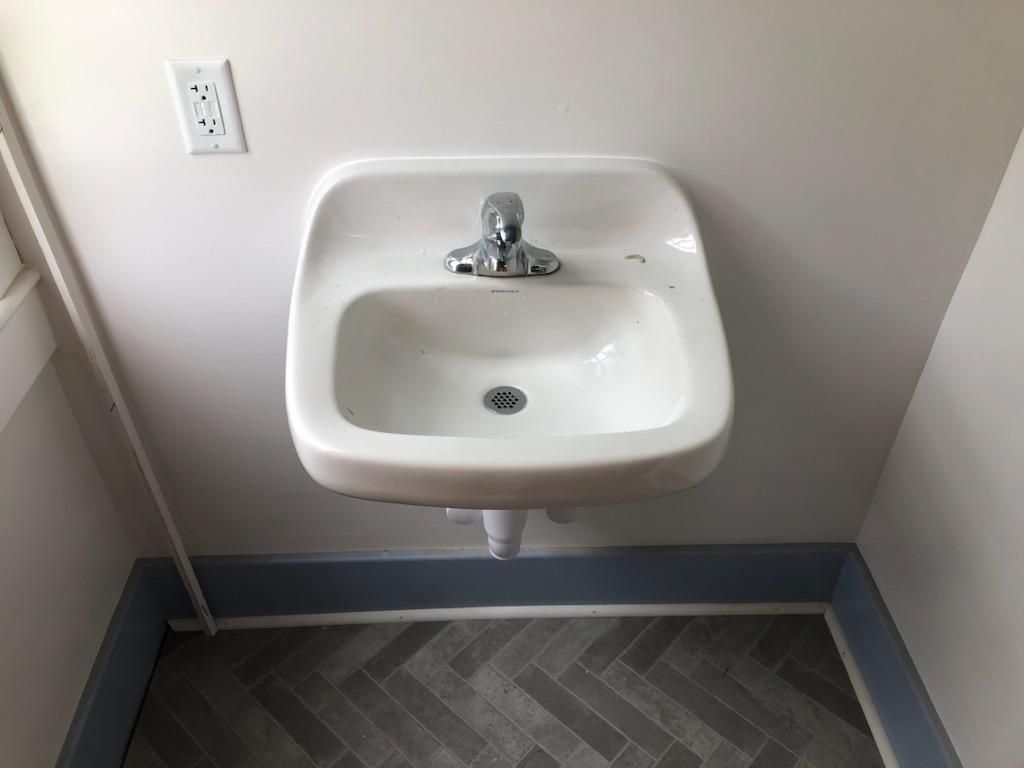 A white sink is hanging on a white wall in a bathroom.