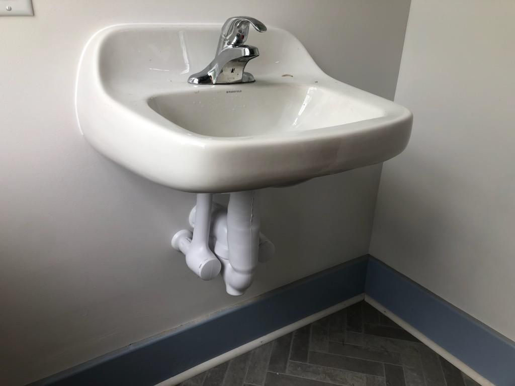 A white sink with a chrome faucet is hanging on a wall in a bathroom.