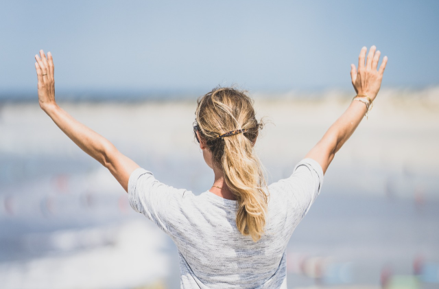Girl facing the ocean with her hand up