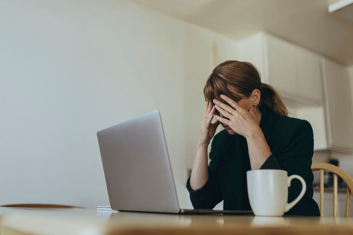 Woman in front of her laptop, hands covering her face